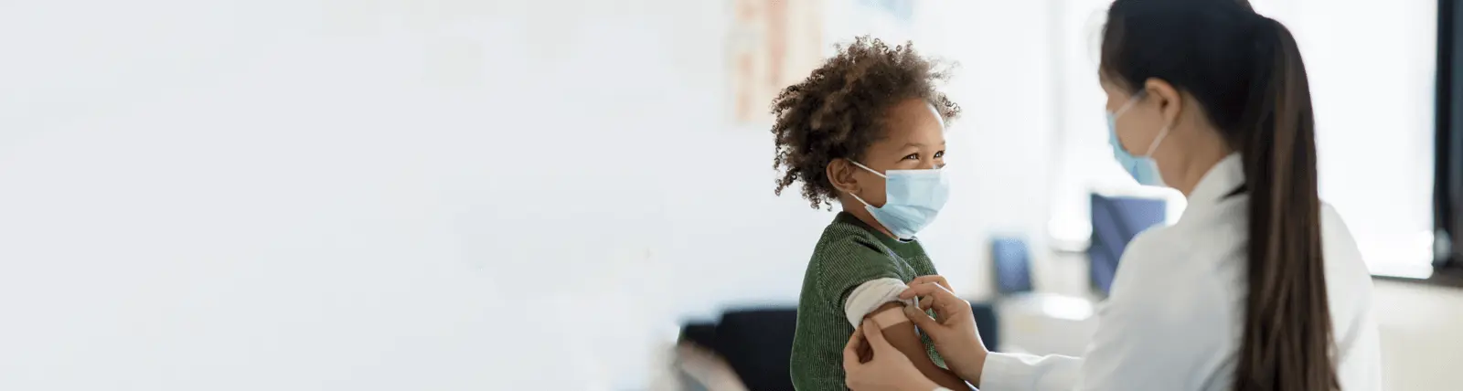 A child smiling after getting a vaccine and band-aid by their doctor