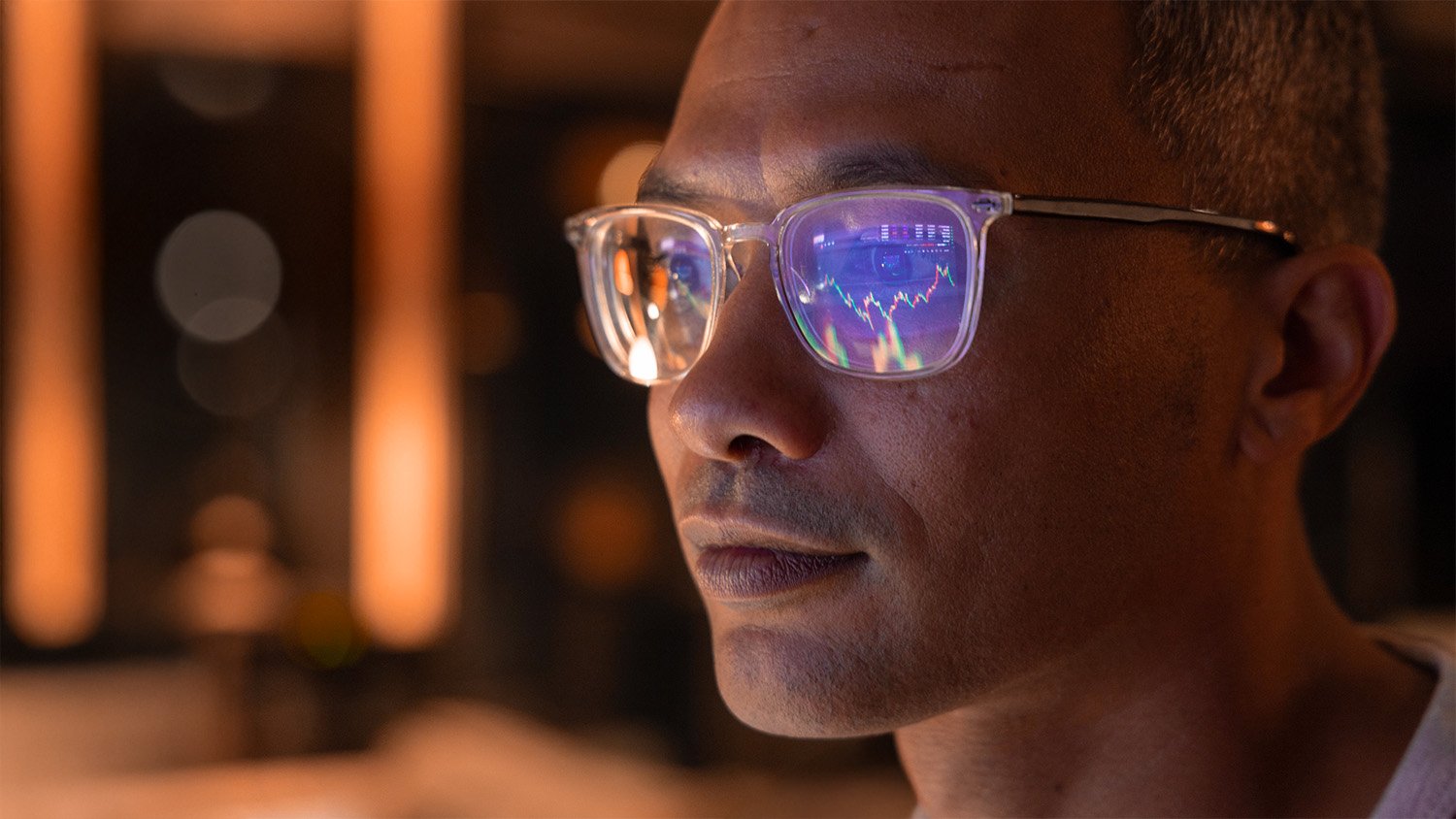 Man gazing offscreen with charts and graphs reflecting in his glasses