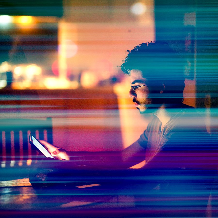 Man sitting at a table with the glow of his mobile device reflecting on his face