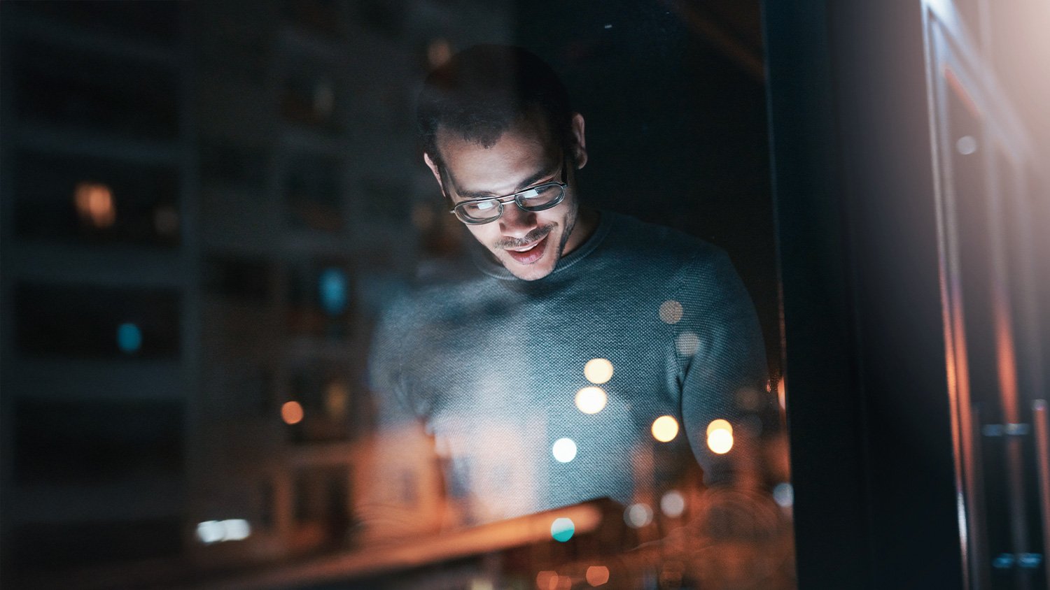 Man looking at a tablet screen illuminating a dark room