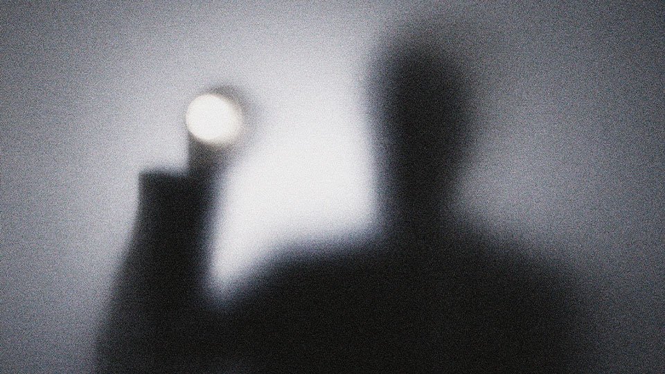 Dark silhouette holding up a flashlight beam