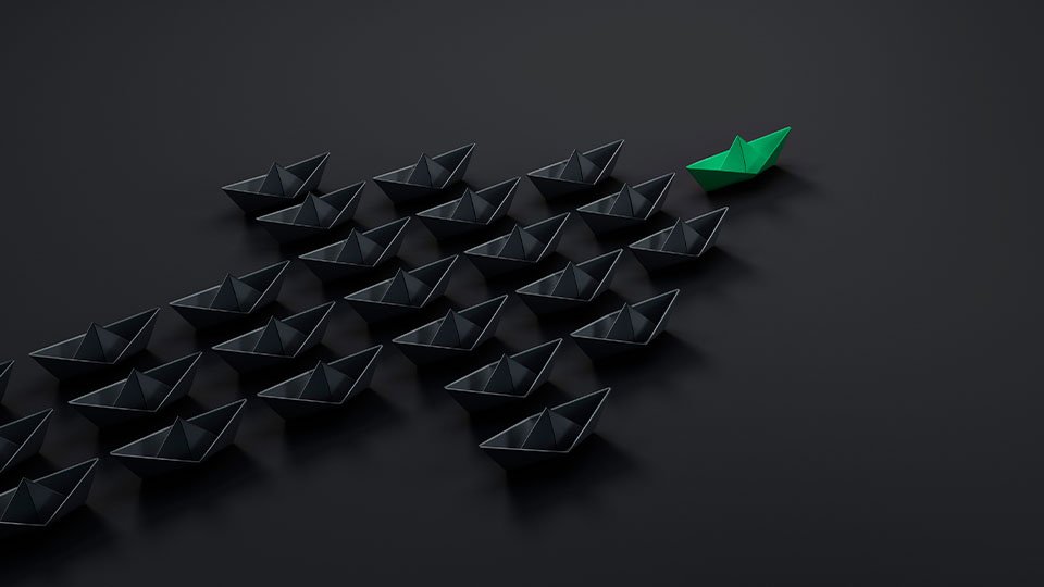 A green paper boat separating itself from the black paper boats
