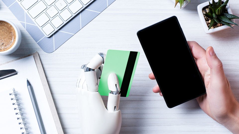 Human hand holding smartphone alongside mechanical hand holding a credit card