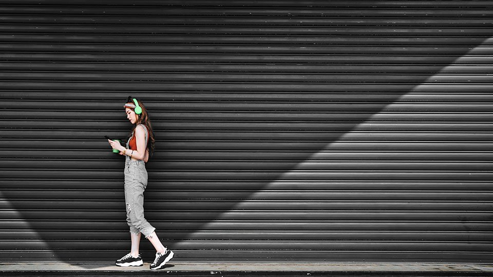 A Woman walking and looking at their cellphone with green headphones on