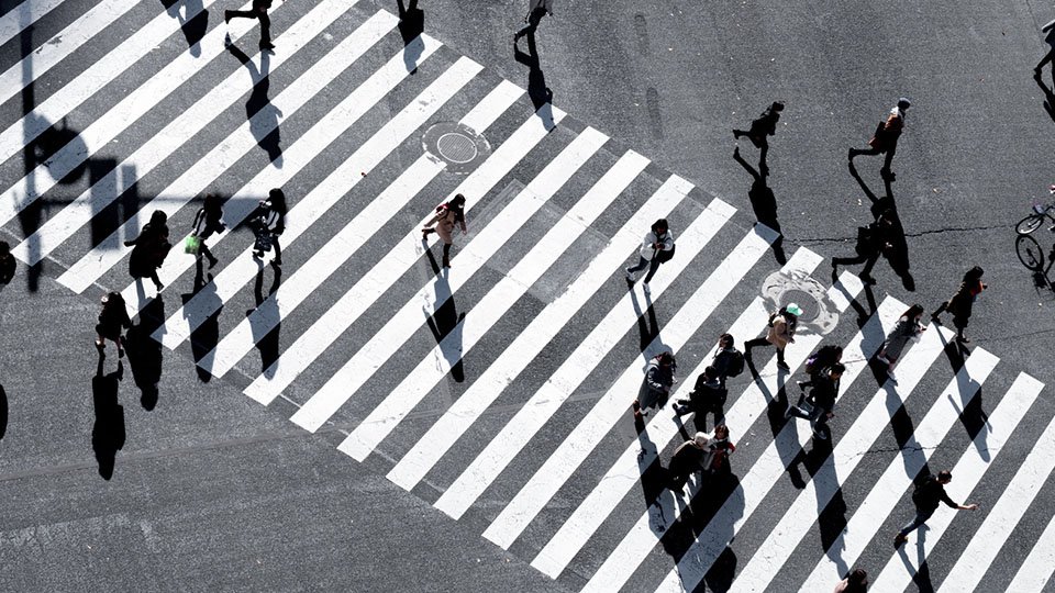 Many pedestrians walking across a striped crosswalk