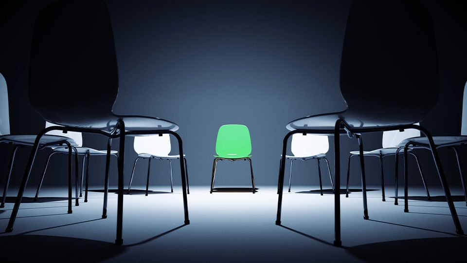 A green chair at the center of a ring of neutral chairs.